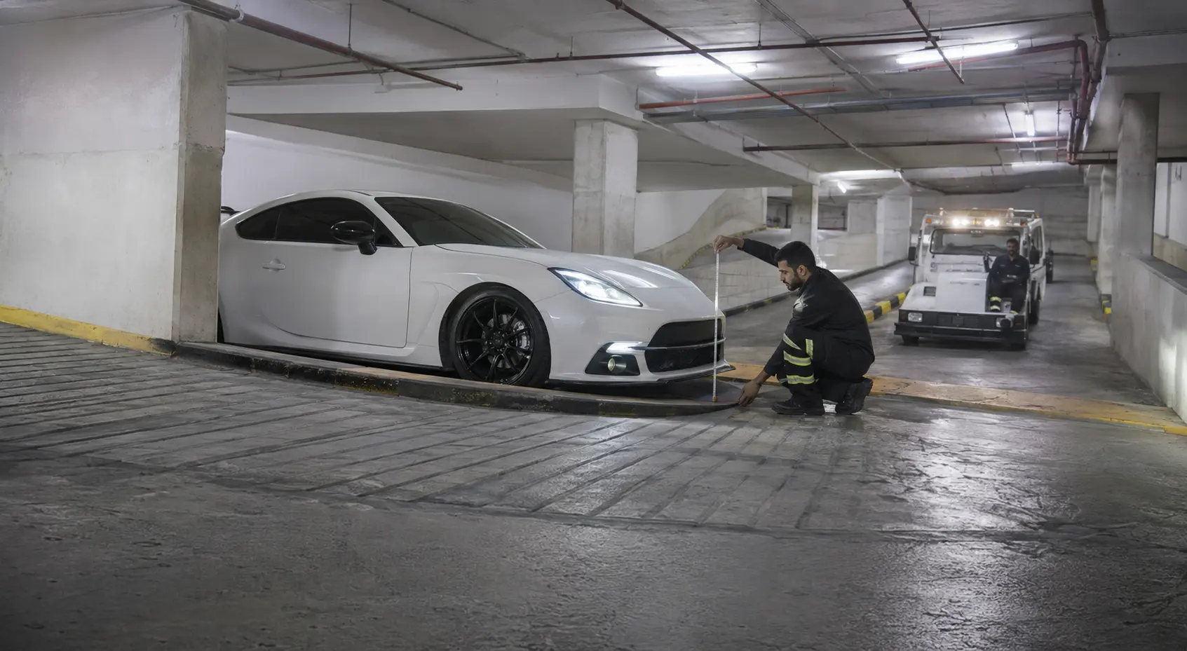 Technicians measuring basement clearance and ramp access around a low sports car